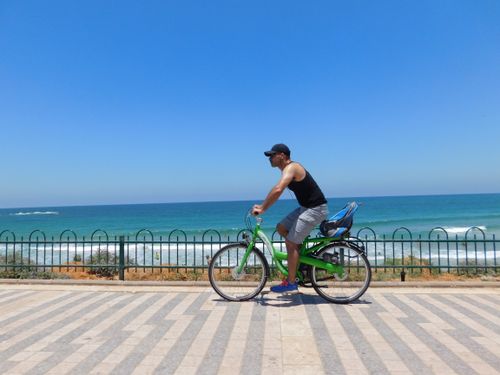 Free A man rides a bicycle along the Tel Aviv beachfront promenade on a sunny day. Stock Photo