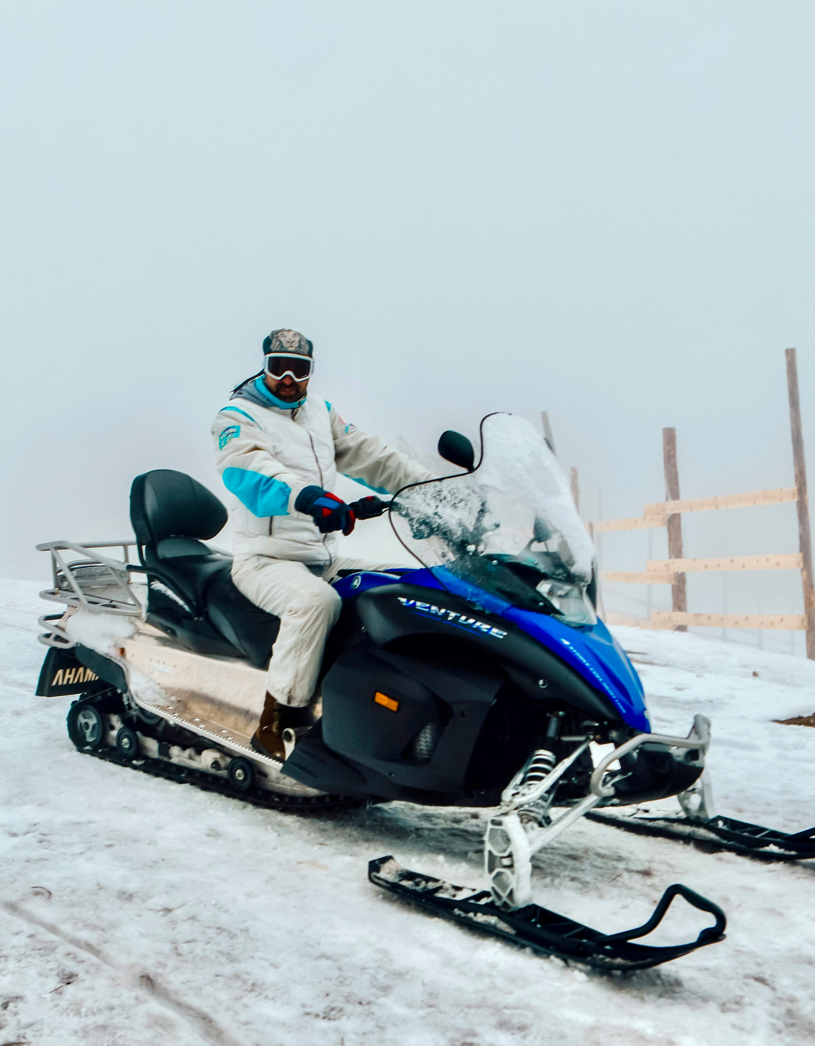A person riding a blue snowmobile on a snowy outdoor landscape during winter, exuding adventure.