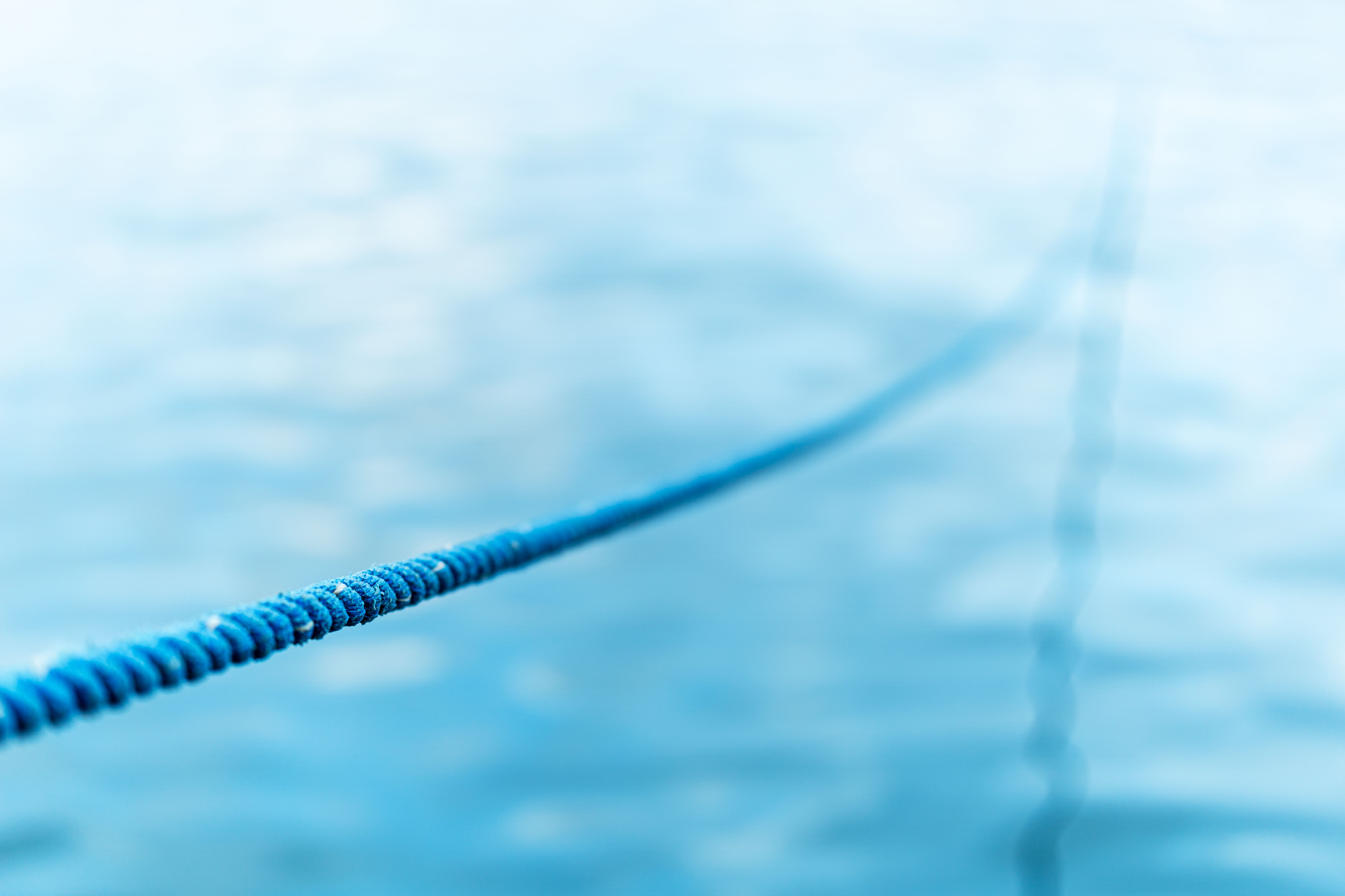 Focused close-up of a blue rope extending over a blurred water background.