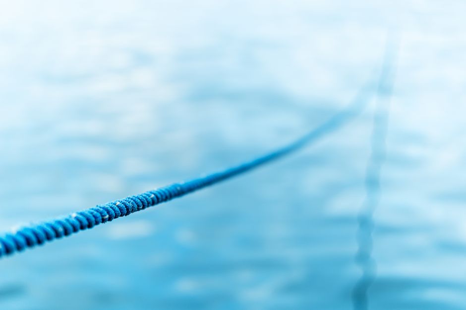 Focused close-up of a blue rope extending over a blurred water background.