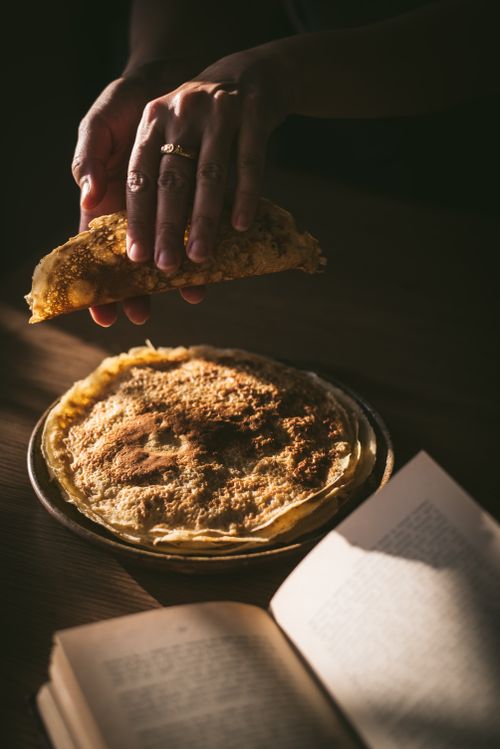 Free Hands preparing crepes with an open cookbook, sunlight casting shadows. Stock Photo