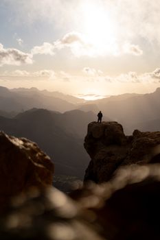 Silhouette of a hiker on a mountain cliff at sunrise, capturing a stunning landscape view.