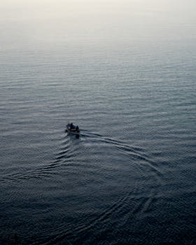 A small boat gracefully navigates the tranquil waters during dusk, creating a peaceful ambiance.