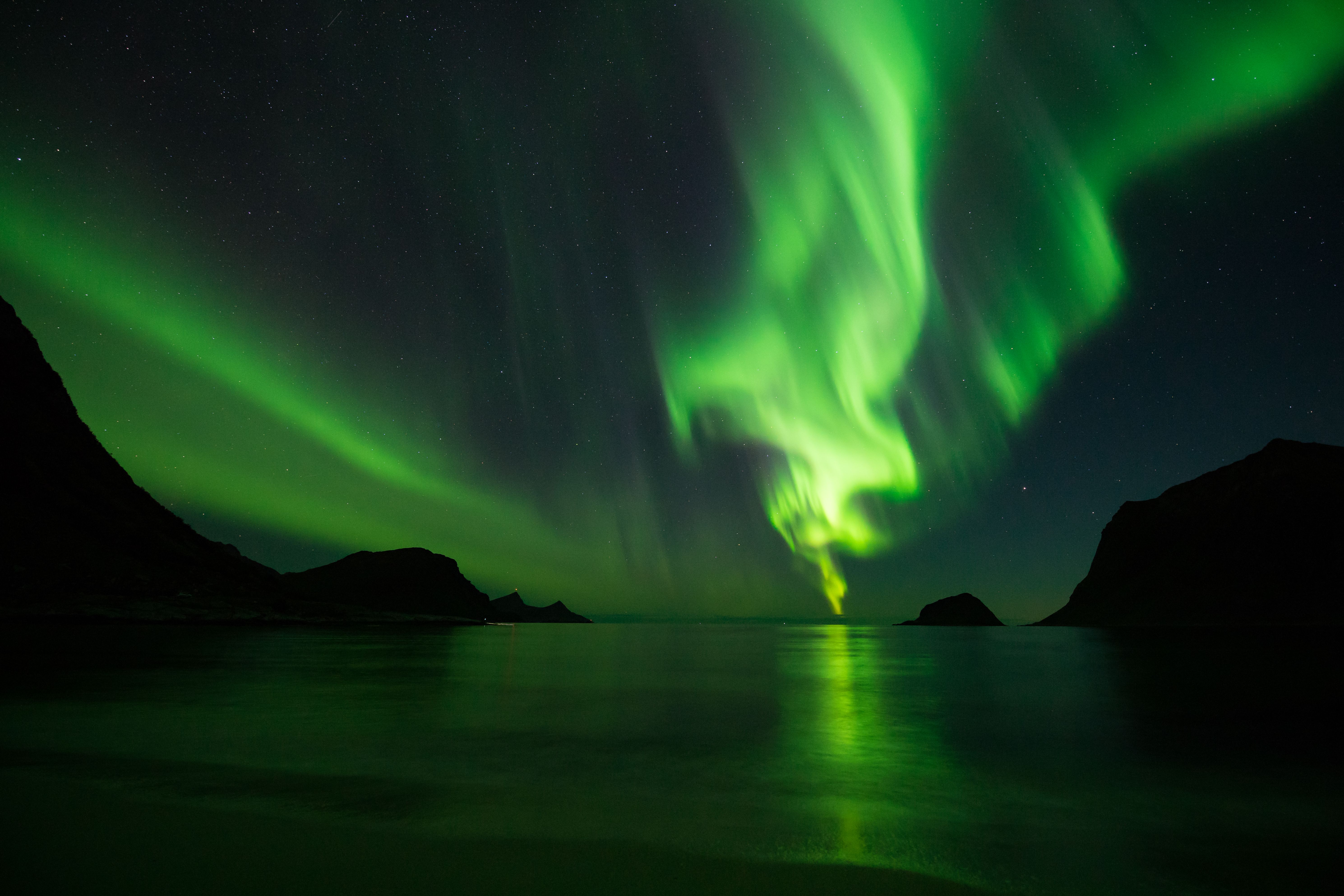 Mesmerizing Northern Lights dance over a tranquil Arctic seascape with silhouetted mountains.