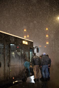 People boarding a bus on a snowy night, city lights in the background creating a moody atmosphere.