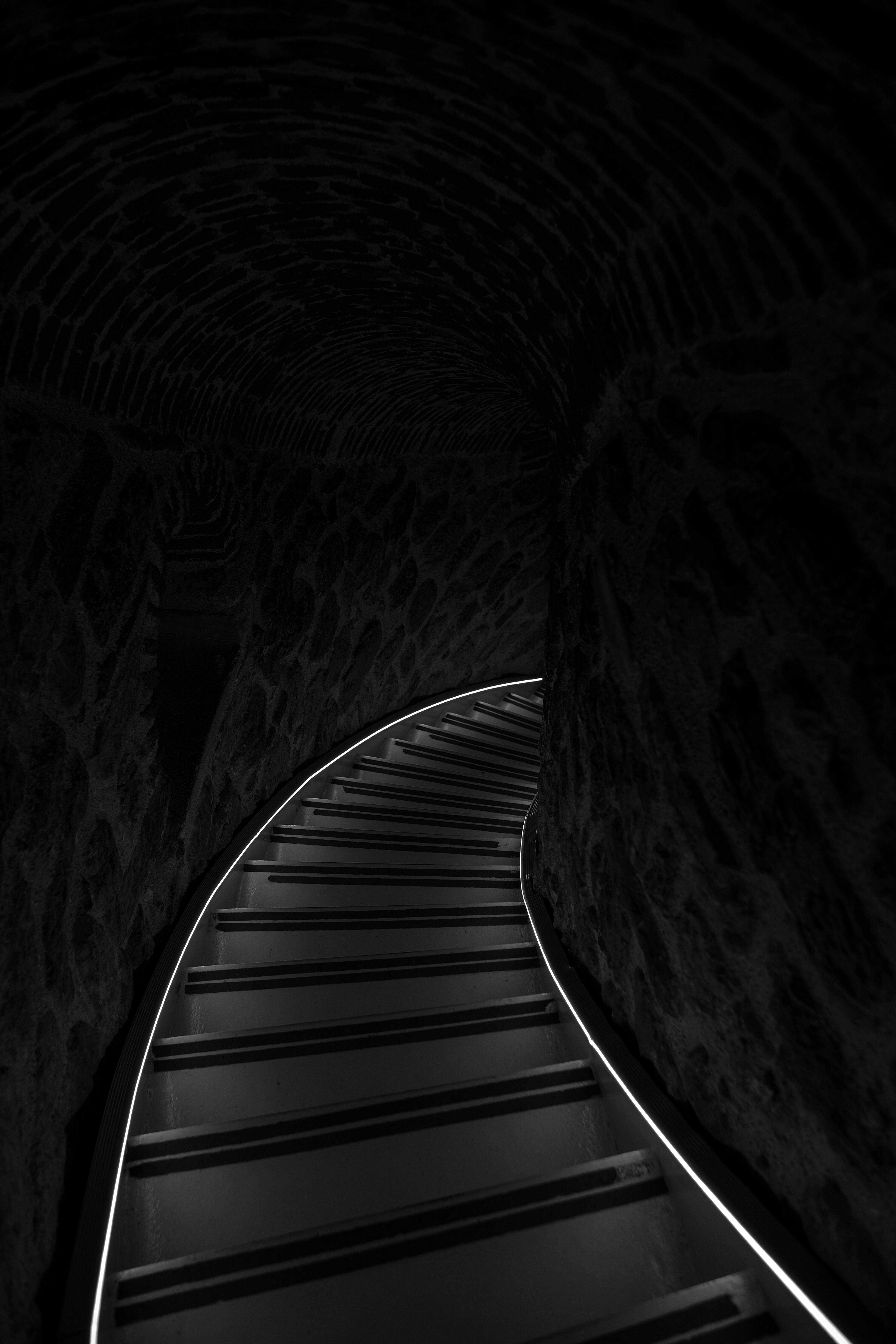 A dramatic black and white shot of a curved staircase in a dark tunnel.