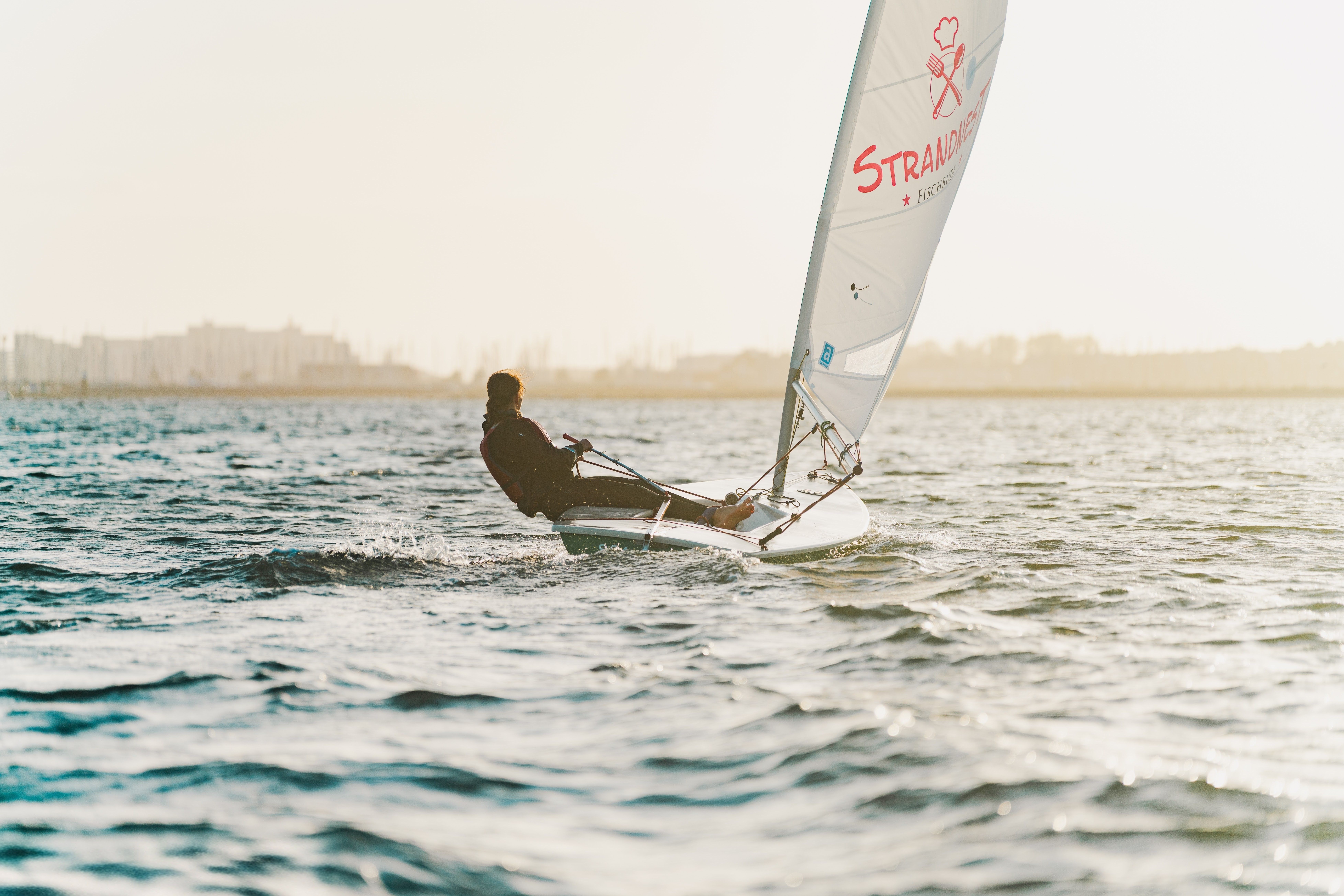 A lone sailor maneuvering a small boat on a sunlit open sea.