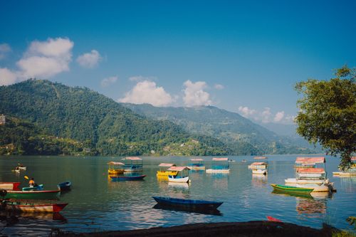 Free Colorful boats on Phewa Lake with lush green hills under clear blue skies. Stock Photo