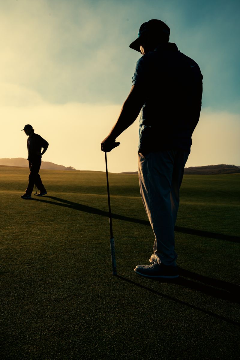 Two golfers casting long shadows on a golf course at sunset