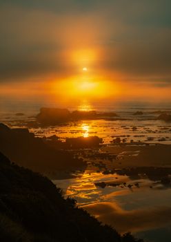 Golden sunset illuminating a rocky seashore, creating a tranquil and dramatic landscape.