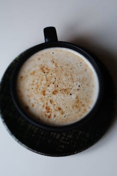 Close-up of a frothy cappuccino in a black cup and saucer, top view.