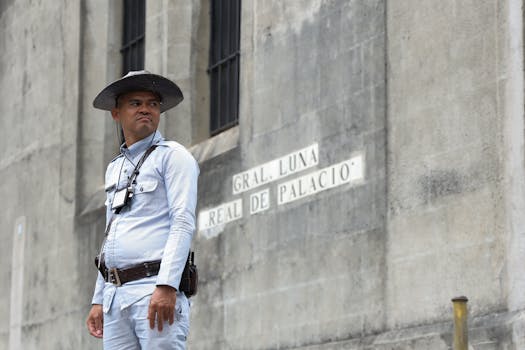 A guard in uniform stands by a historic building in Manila. Street sign reads 'Gral. Luna Real De Palacio'.