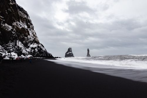 Free Explore the striking Reynisfjara beach with towering basalt stacks and snowy cliffs in a moody winter setting. Stock Photo