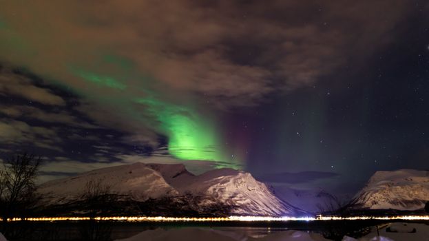 Capture of vibrant Northern Lights illuminating snowy mountains against a starry night sky.
