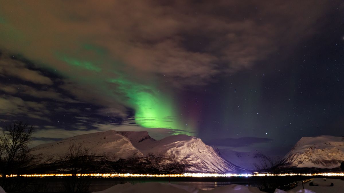 Green Northern Lights illuminating snowy Norwegian mountains against a starry night sky