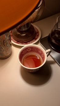 A warm cup of tea on a cozy table setting with a lamp, perfect for a calming evening indoors.