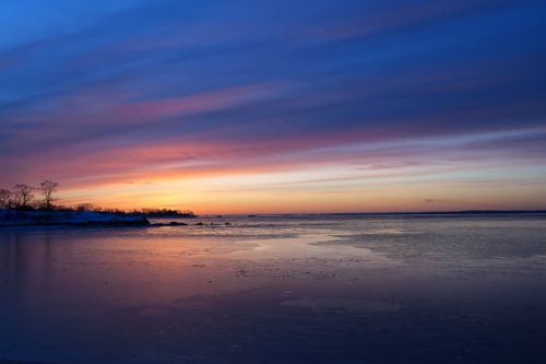 Free Stunning winter sunset casting vibrant colors over a calm, frozen lake with a peaceful horizon. Stock Photo