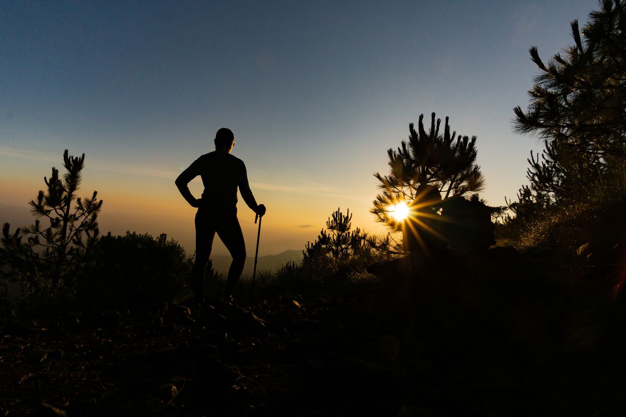 Silhouette of a hiker at sunrise against a dramatic mountain landscape