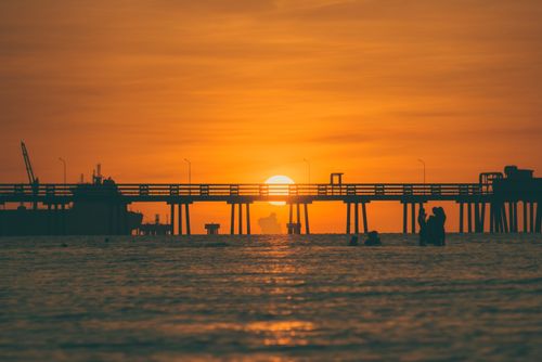Free A serene sunset over the ocean with a pier silhouetted, evoking calm and tranquility. Stock Photo