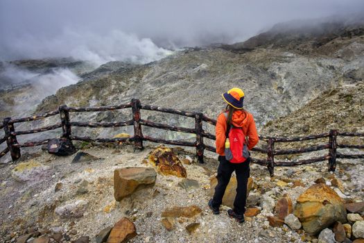 Hiker in vibrant attire gazing at misty volcanic landscape in Jawa Barat, Indonesia.
