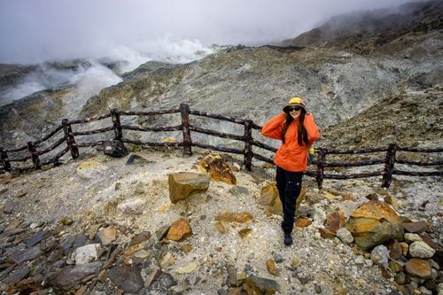 Free Woman in orange jacket hiking a rocky volcanic terrain in Indonesia. Stock Photo