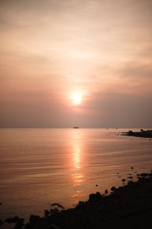 Free Serene sunset over a calm sea with warm hues reflecting on the water, ideal for peaceful ambiance. Stock Photo