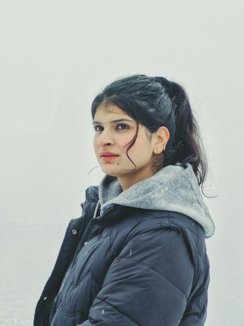 Free A young woman in a winter coat stands outdoors in a snowy landscape, gazing thoughtfully. Stock Photo