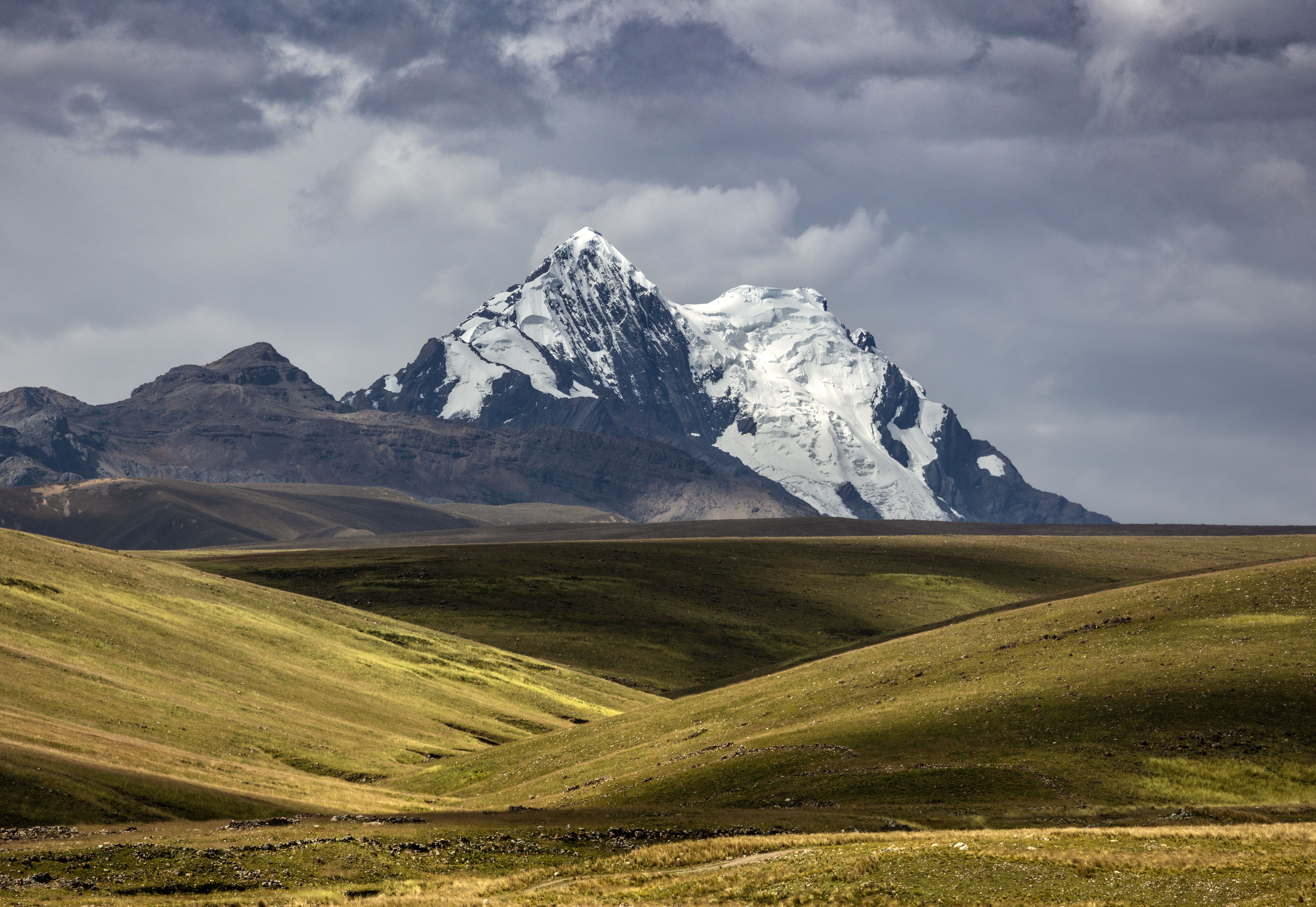 Stunning view of a snow-capped mountain in the Cordillera Blanca, Peru, with rolling meadows in the foreground.