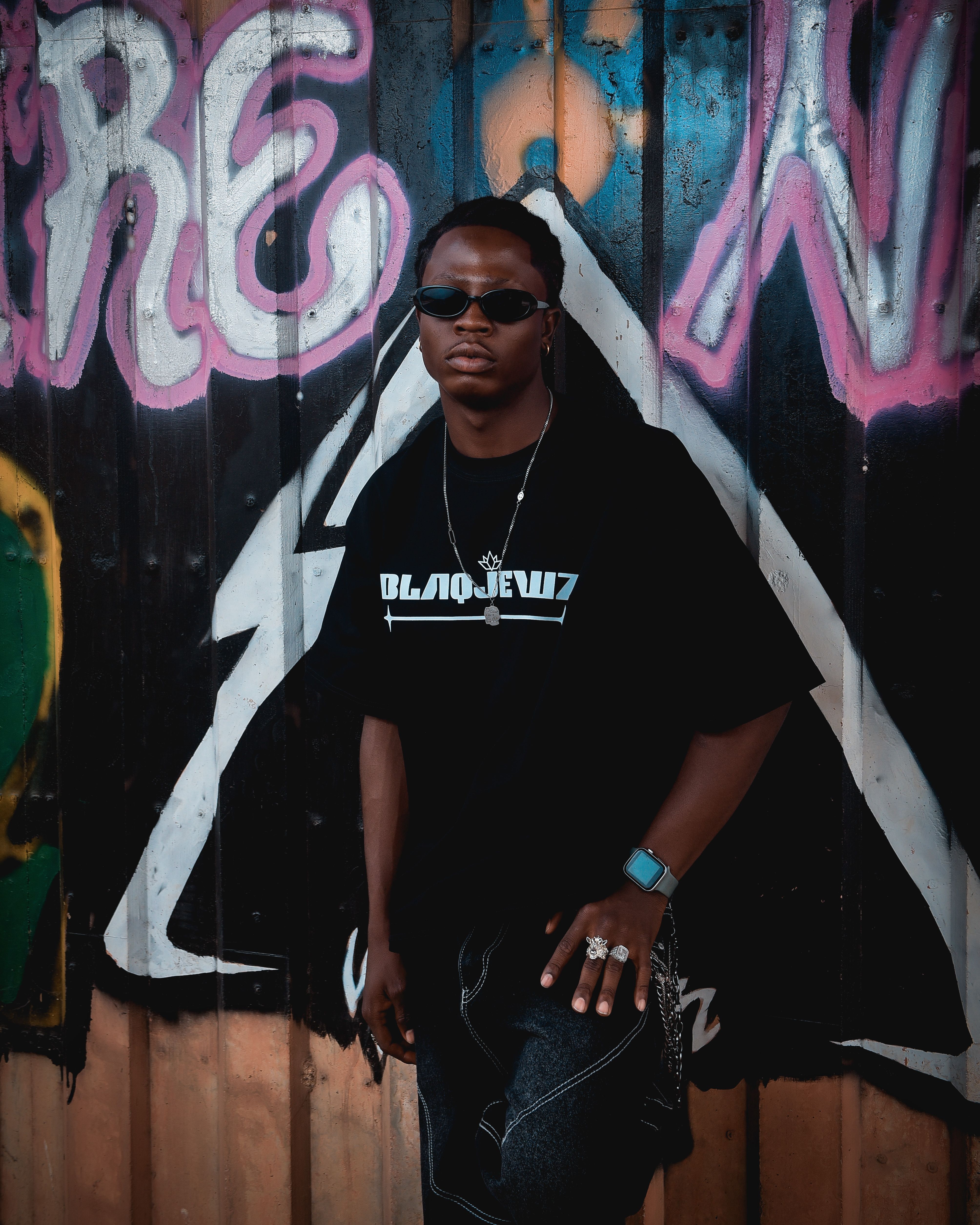 Stylish young adult in black attire against vibrant graffiti wall.