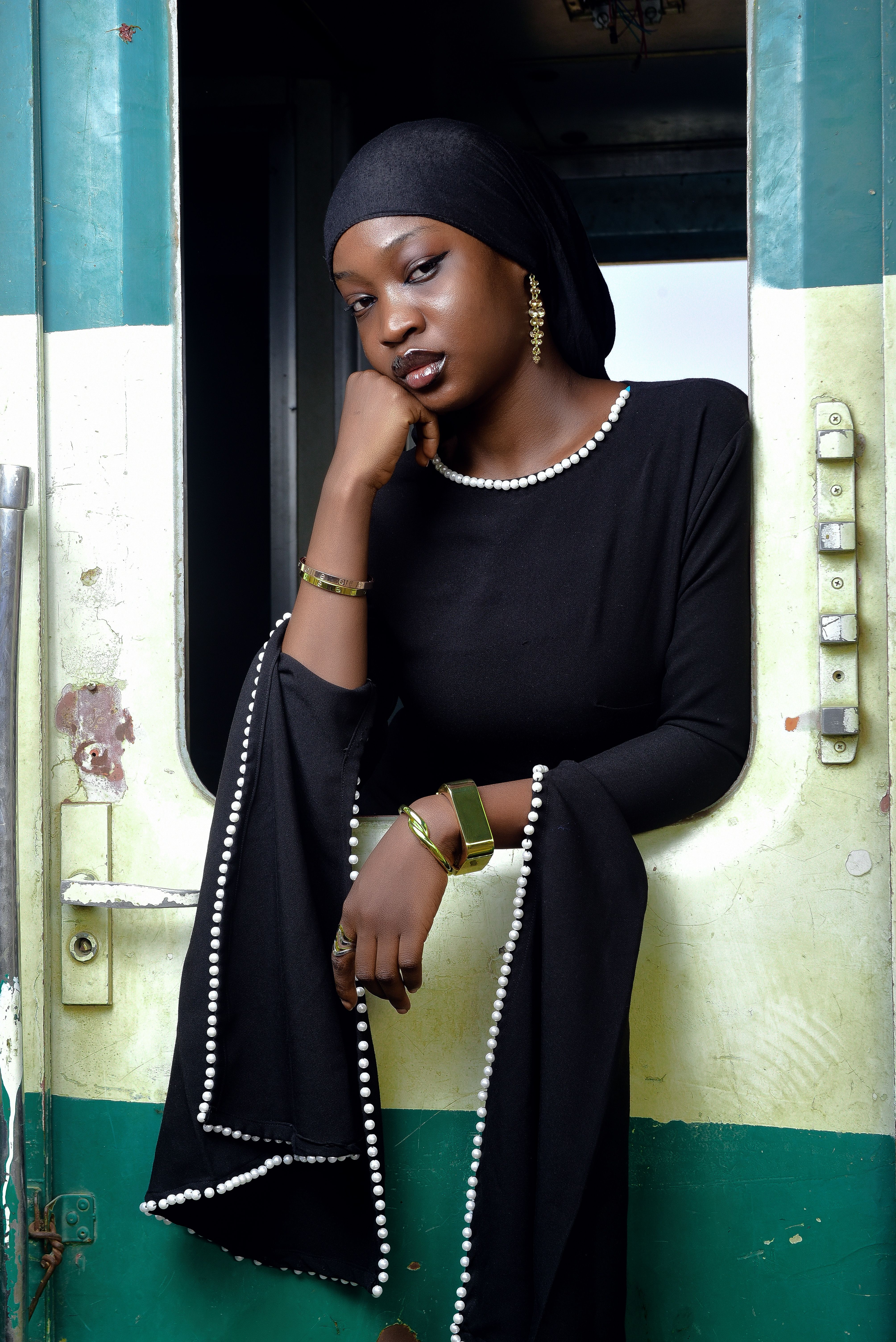 Stylish woman in black dress with pearl details posing in a train compartment window.