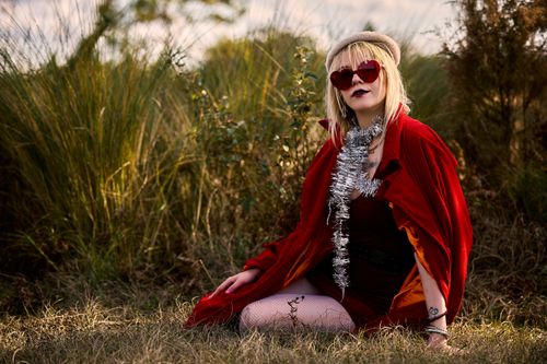 Free Stylish woman in a red cape and sunglasses posing in a grassy field with a festive vibe. Stock Photo