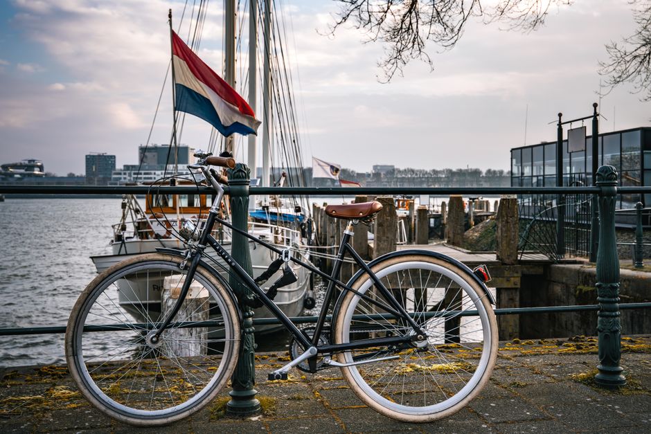 A bicycle parked by a harbor in the Netherlands with boats and the Dutch flag visible.