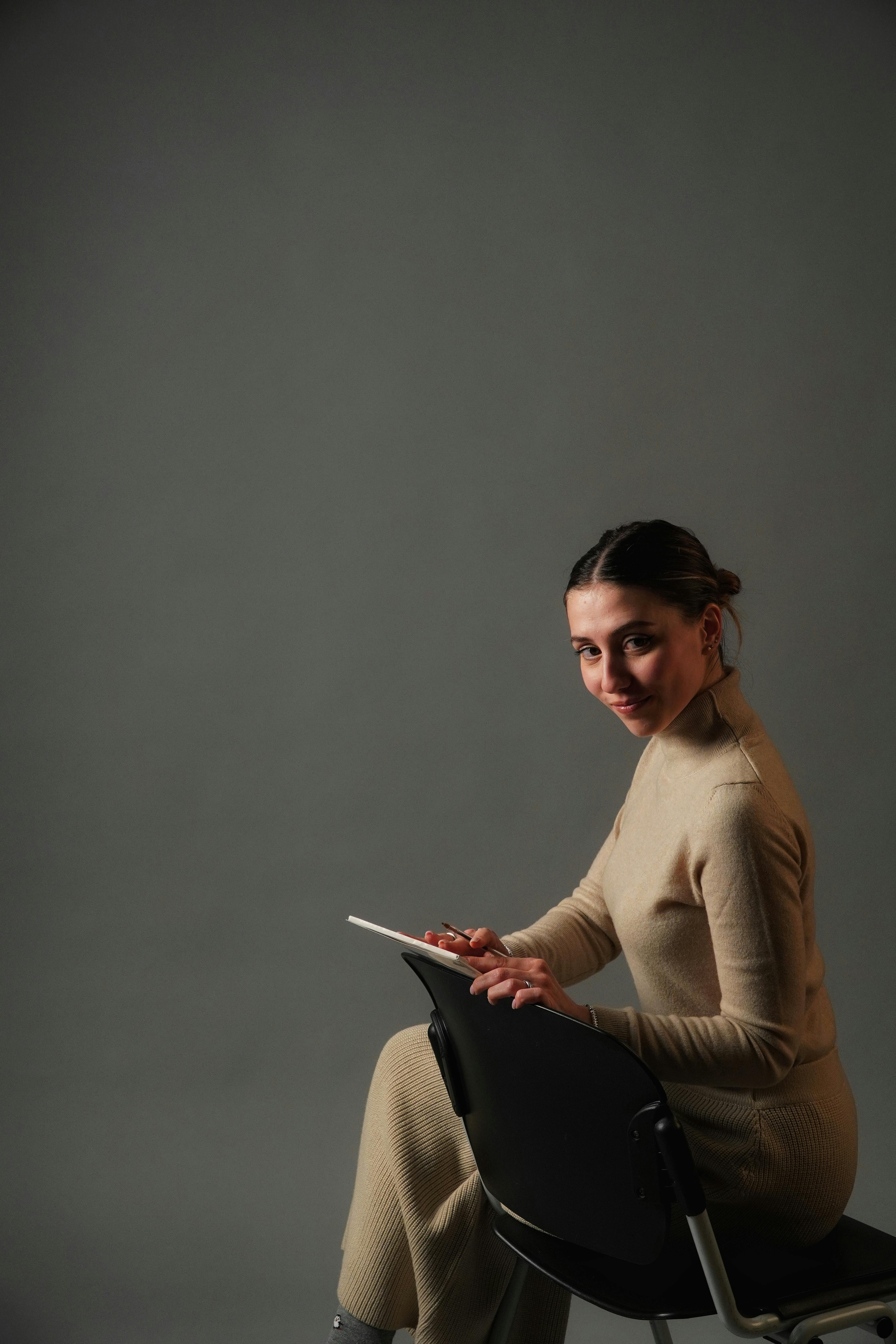 Ilmainen Beigenväriseen asuun pukeutunut nainen poseeraa tabletin kanssa yksinkertaista harmaata studiotaustaa vasten. Kuvapankkikuva