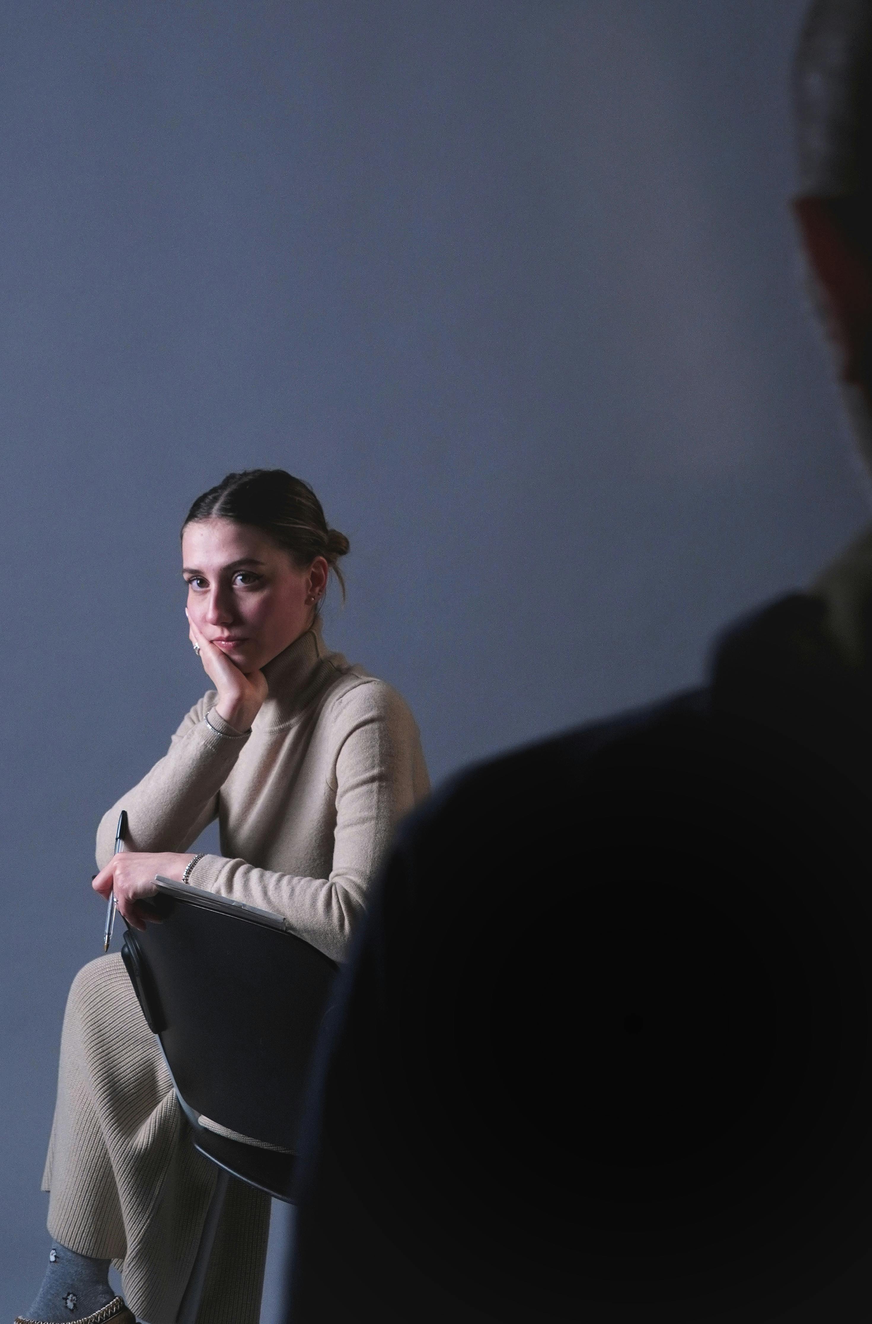 Безкоштовне Жінка задумливо сидить у приміщенні з м'яким освітленням, створюючи безтурботний та інтроспективний настрій. стокове фото