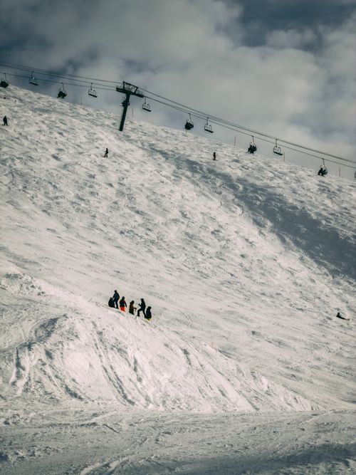 Free A group of skiers navigate a snowy slope below a chairlift under cloudy skies. Stock Photo