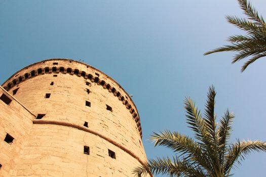 A historic round tower and palm trees with a clear blue sky, showcasing Egyptian architecture.