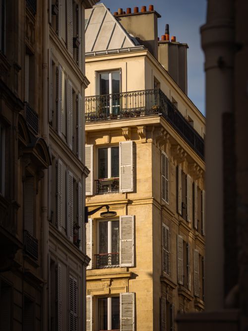 Free A sunlit street scene featuring classic Parisian architecture with traditional shutters and balconies. Stock Photo