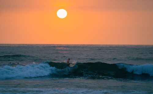 Free A surfer catches a wave under a vibrant sunset, perfect for adventure seekers. Stock Photo