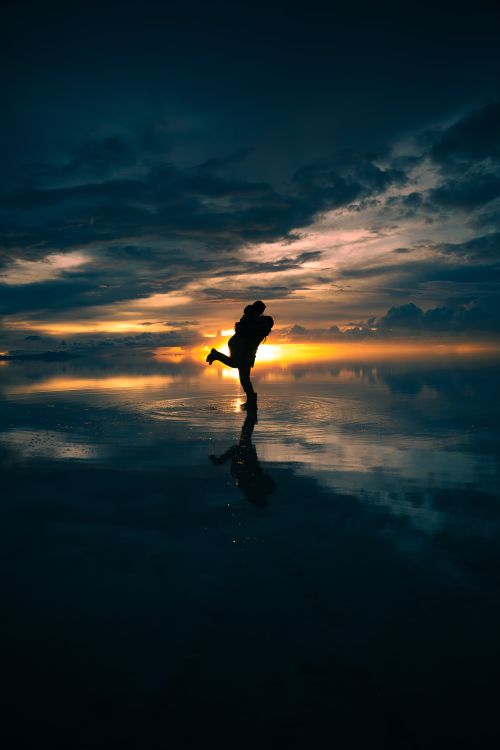 Free Silhouette of a couple embracing during a stunning sunset at Salar de Uyuni, Bolivia. Stock Photo