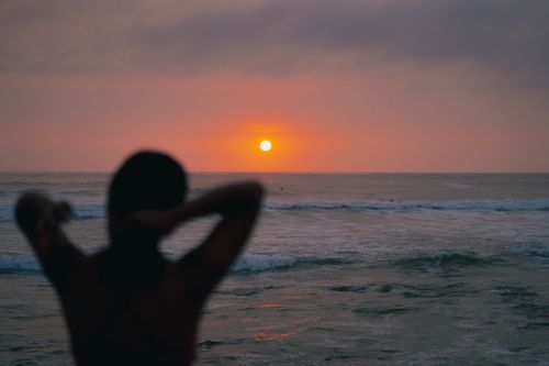 Free A person silhouetted against a vibrant ocean sunset, creating a peaceful scene. Stock Photo