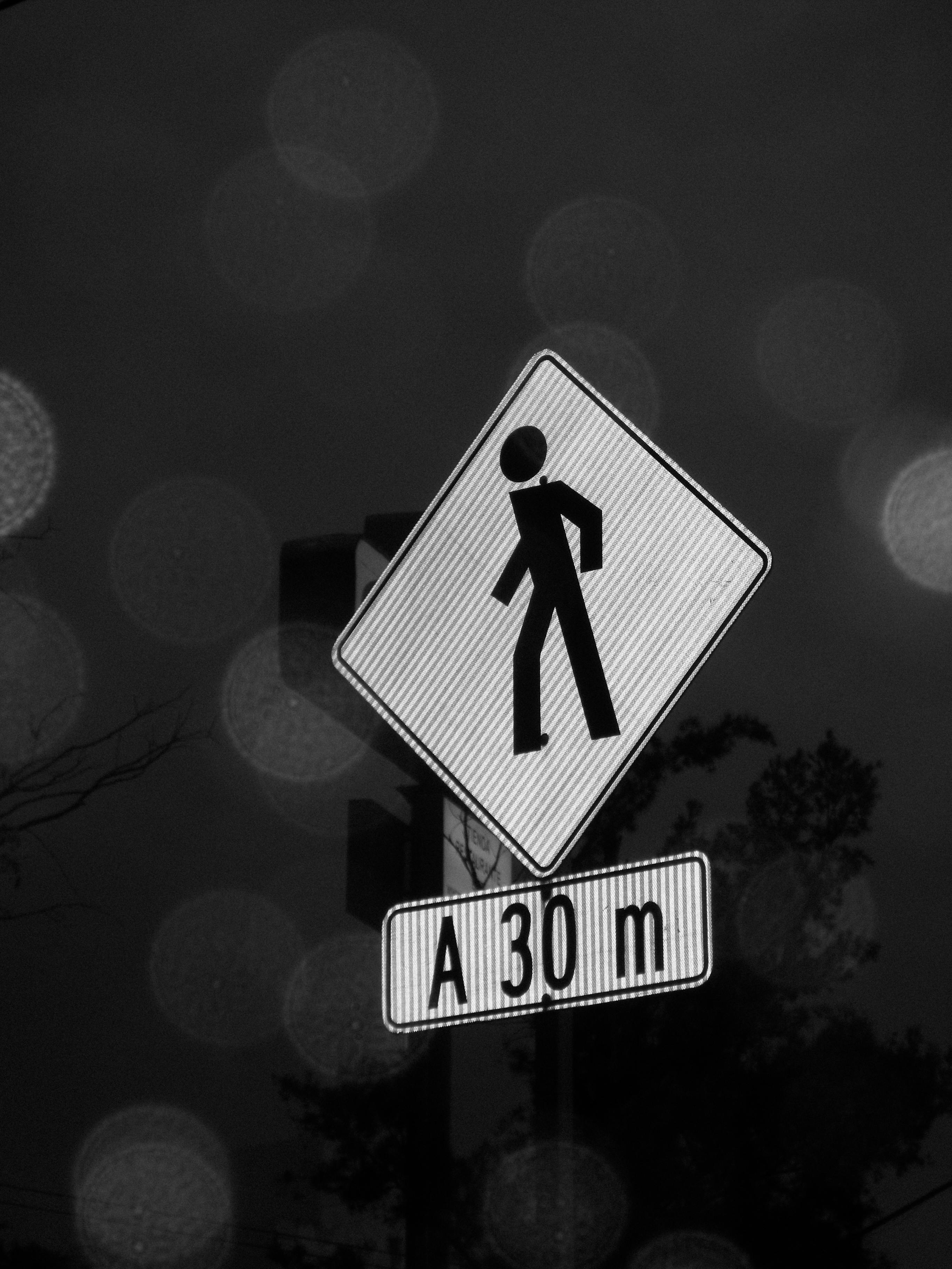 Gratis Foto in bianco e nero di un segnale di attraversamento pedonale con effetto bokeh di notte. Foto a disposizione