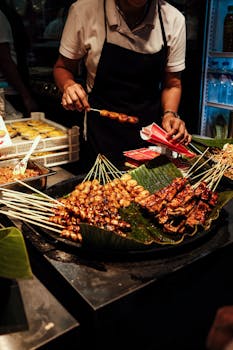 Grilled chicken and sausage skewers being prepared by a vendor at a bustling night market in Manila.