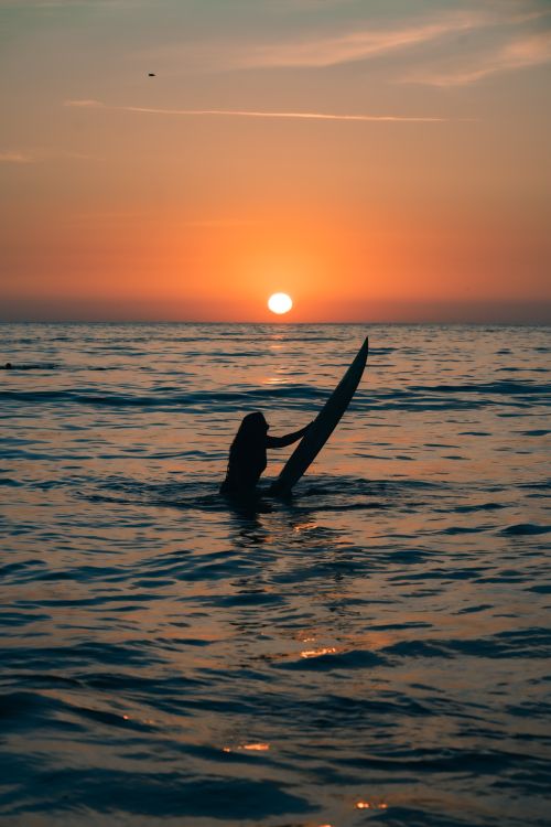 Free Silhouette of a surfer holding a board during a vibrant ocean sunset. Stock Photo