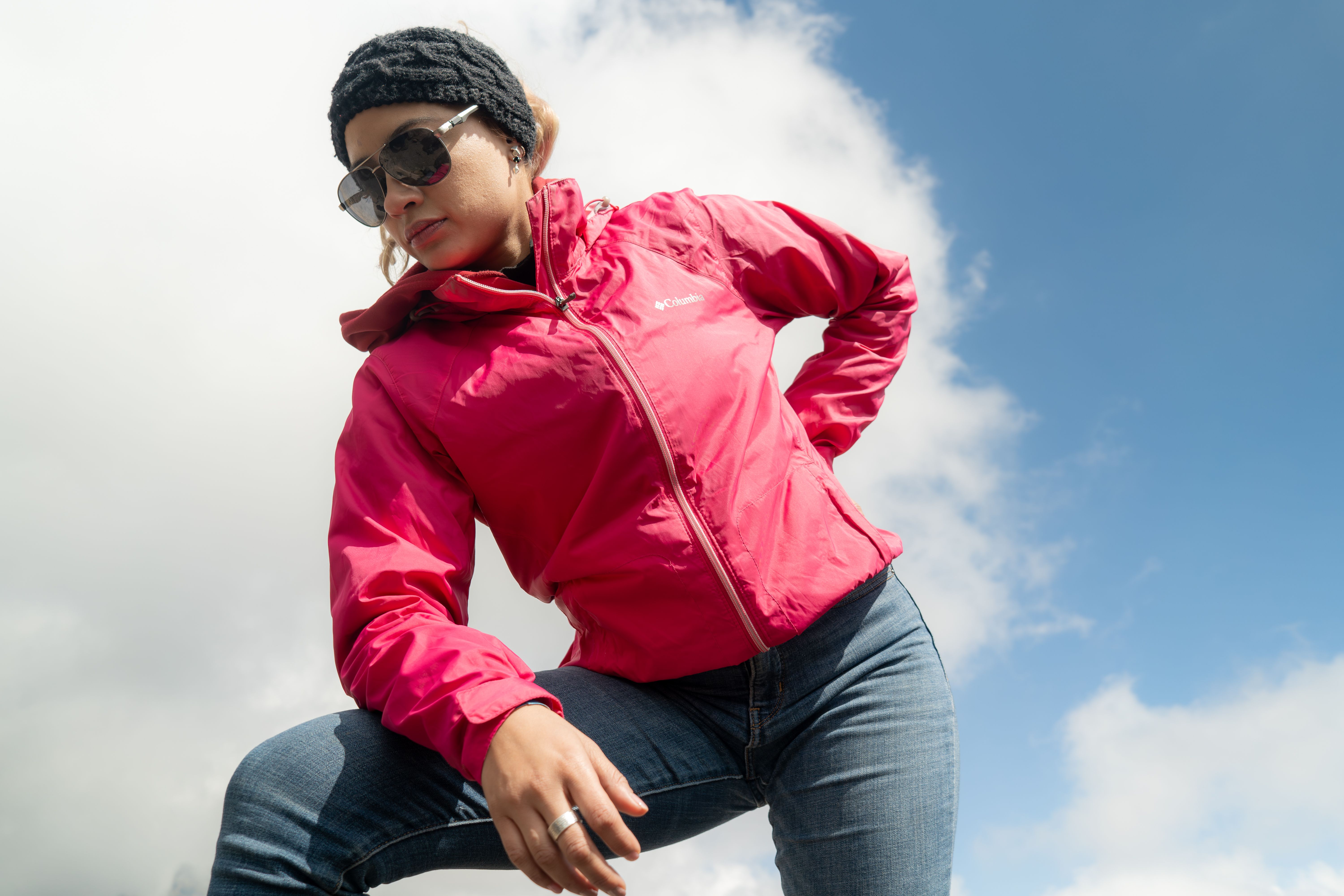 Confident woman in pink jacket posing under a bright blue sky.