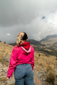 A woman in vibrant attire explores a mountain path under cloudy skies.
