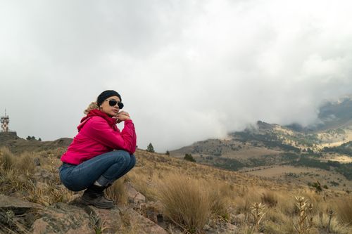 Free A woman in a red jacket enjoys a foggy mountain view, showcasing adventure and nature's beauty. Stock Photo