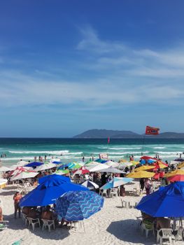 Vibrant beach scene with colorful umbrellas and crowds in Cabo Frio, Brazil. Perfect summer getaway.
