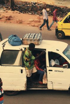 A packed minivan on a bustling street, showcasing urban life in a developing area.