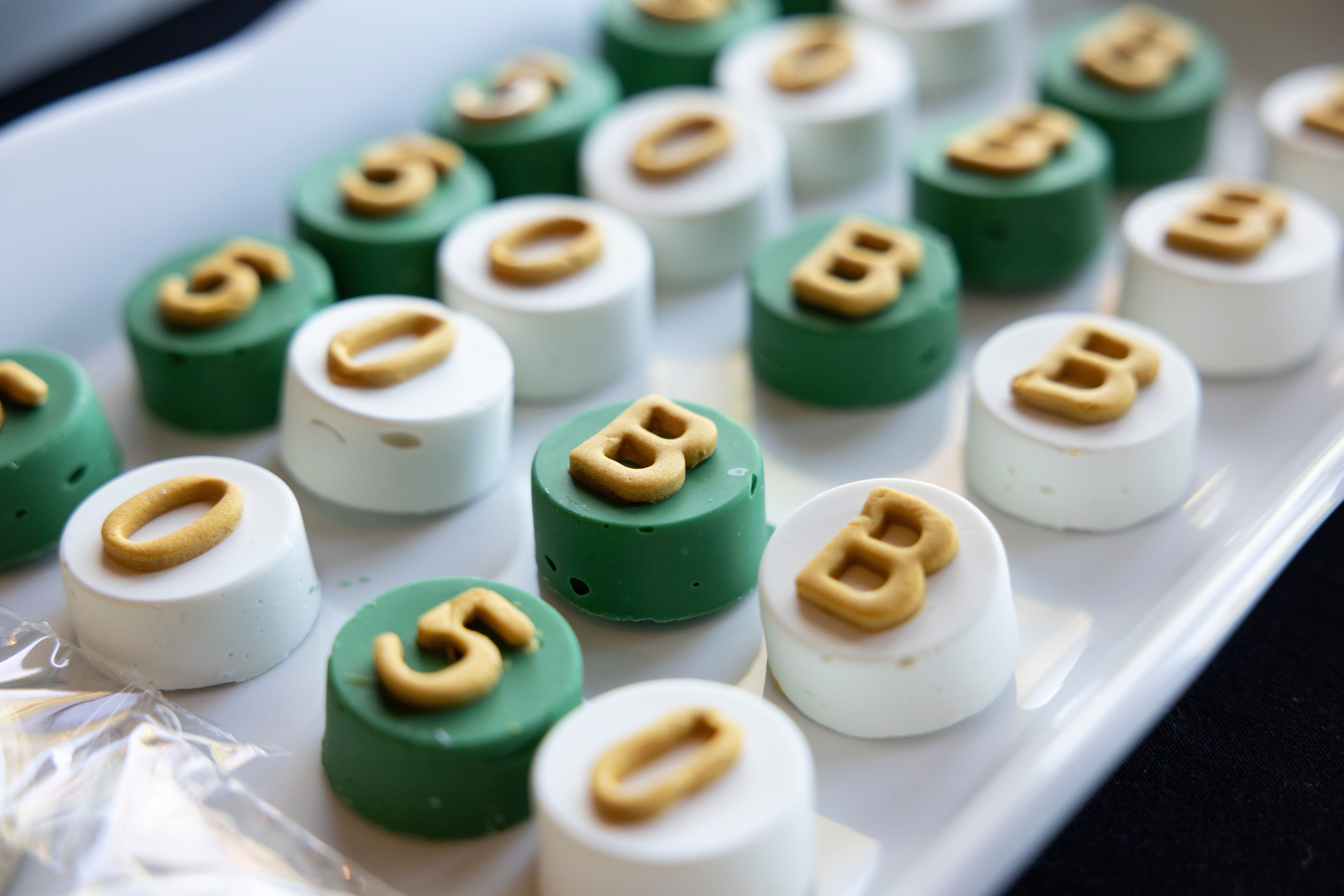 Close-up of decorative green and white macarons with alphabet design on a serving tray.