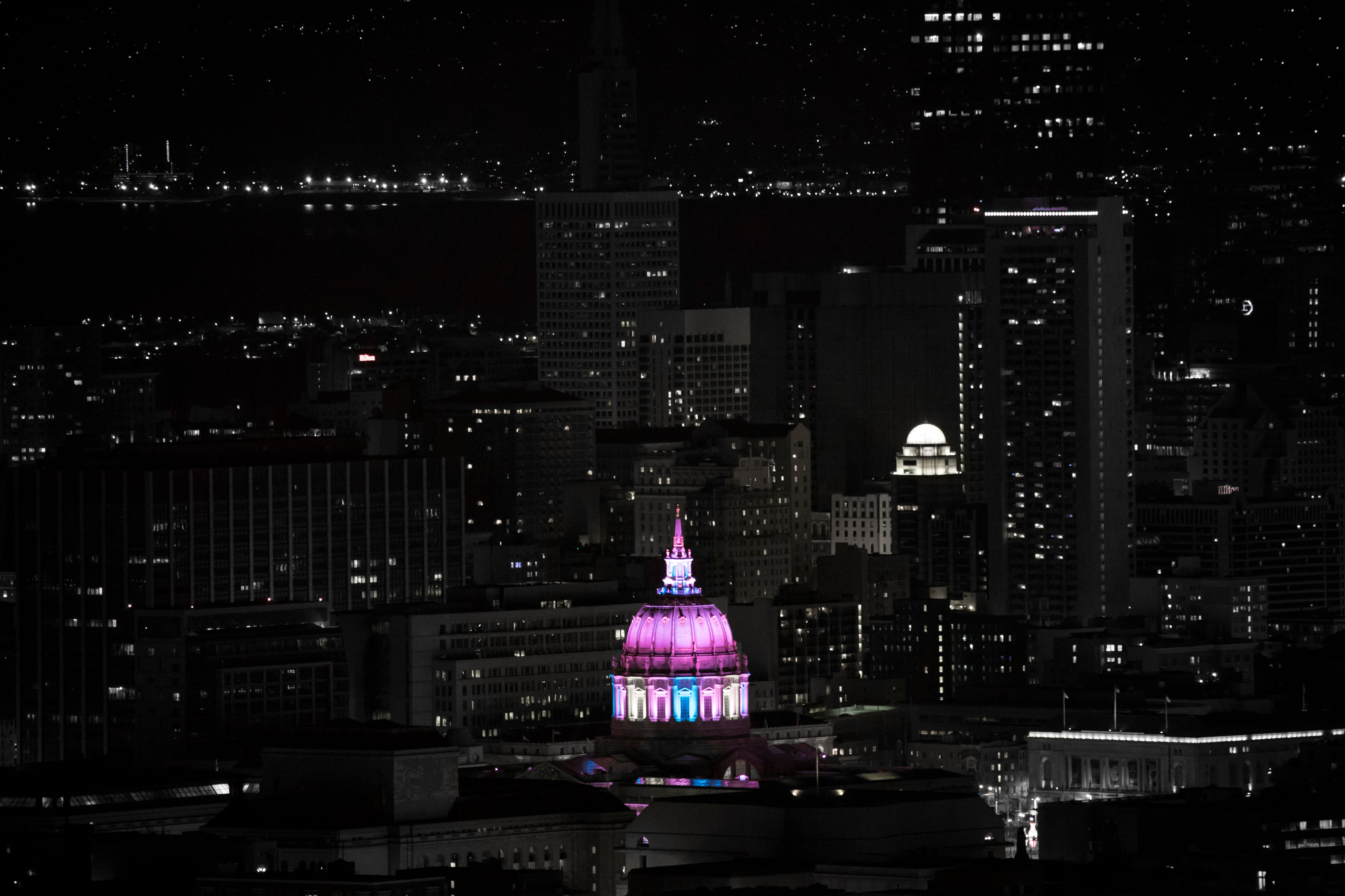 San Francisco City Hall brightly lit in pink and purple during nighttime cityscape.